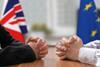 Two men facing each other at a table with EU and UK flags in the background