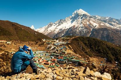 A man sits on a Nepalese mountainside with his head in his hands - apparently suffering from altitude sickness