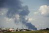 A photo of smoke rising from a plant behind some shops on a road