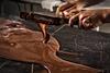 A photo of a person's hands holding two long spatulas covered in melted chocolate. The chocolate is dripping off the spatulas and pooling on a marble surface underneath, which is covered in more molten chocolate.