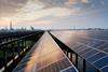 A photo of solar panels during sunset on a bright day. There's an industrial complex in the far distance