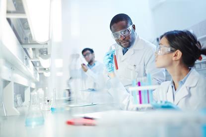 Scientists in labcoats and PPE examine test tubes