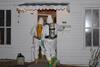 Two figures in white hazmat suits with breathing apparatus enter through the door of a rundown house