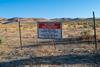 A landscape of dry mountainous grassland with clear blue sky. A sign in on a barb wire fence in the foreground says: Access Restricted/ Active Mine Site/Thacker Pass Project/ For access please call Lithium Nevada Corp