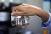 A hand in a lab coat holds up three vials of THC and CBD