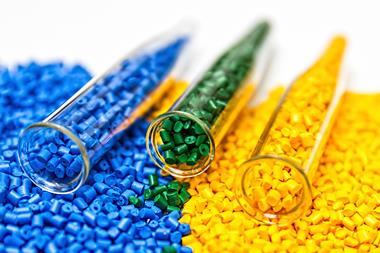 Close-up of chemistry vials or test-tubes containing thermoset plastic pellets in blue, green and yellow, spilling out onto the foreground