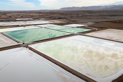 An overhead view of large green and white square salty pools in a desert environment