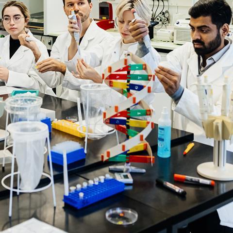 A cluttered lab bench full of apparatus slightly obscures the students working at it, as they perform an experiment as part of their training