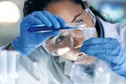 Close up of a young female scientist pouring a blue chemical from a vial into a round bottom flask