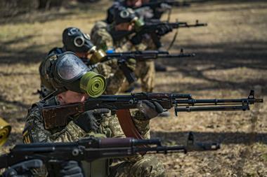 Soldiers aiming rifles with their gas masks pushed to the top of their heads.